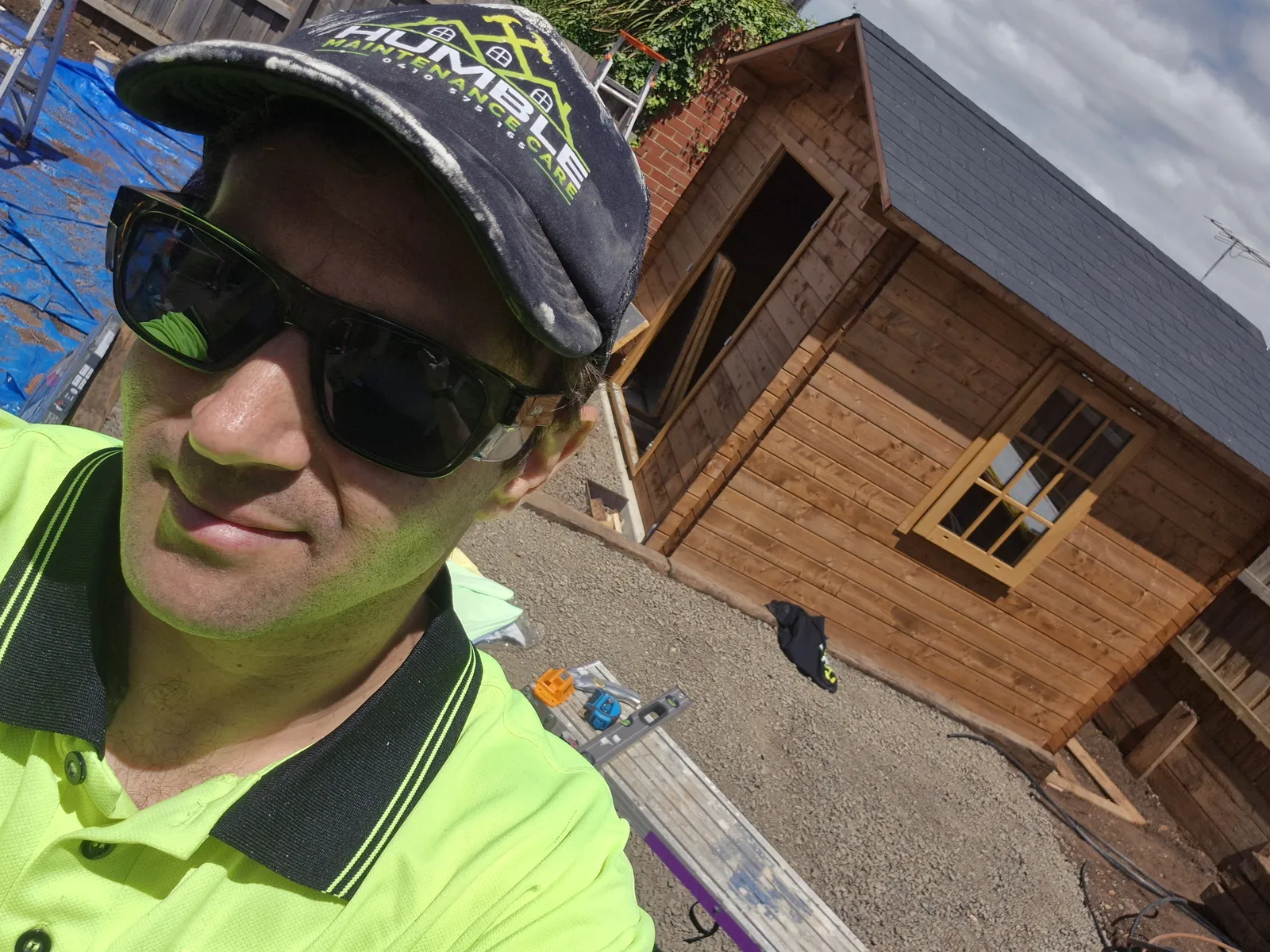 Karl on-site in his Humble cap with the freshly shingled cabin behind him