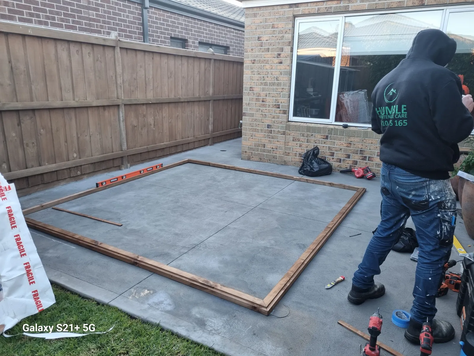 Karl in his Humble Maintenance Care hoodie marking out the cabin frame on the slab