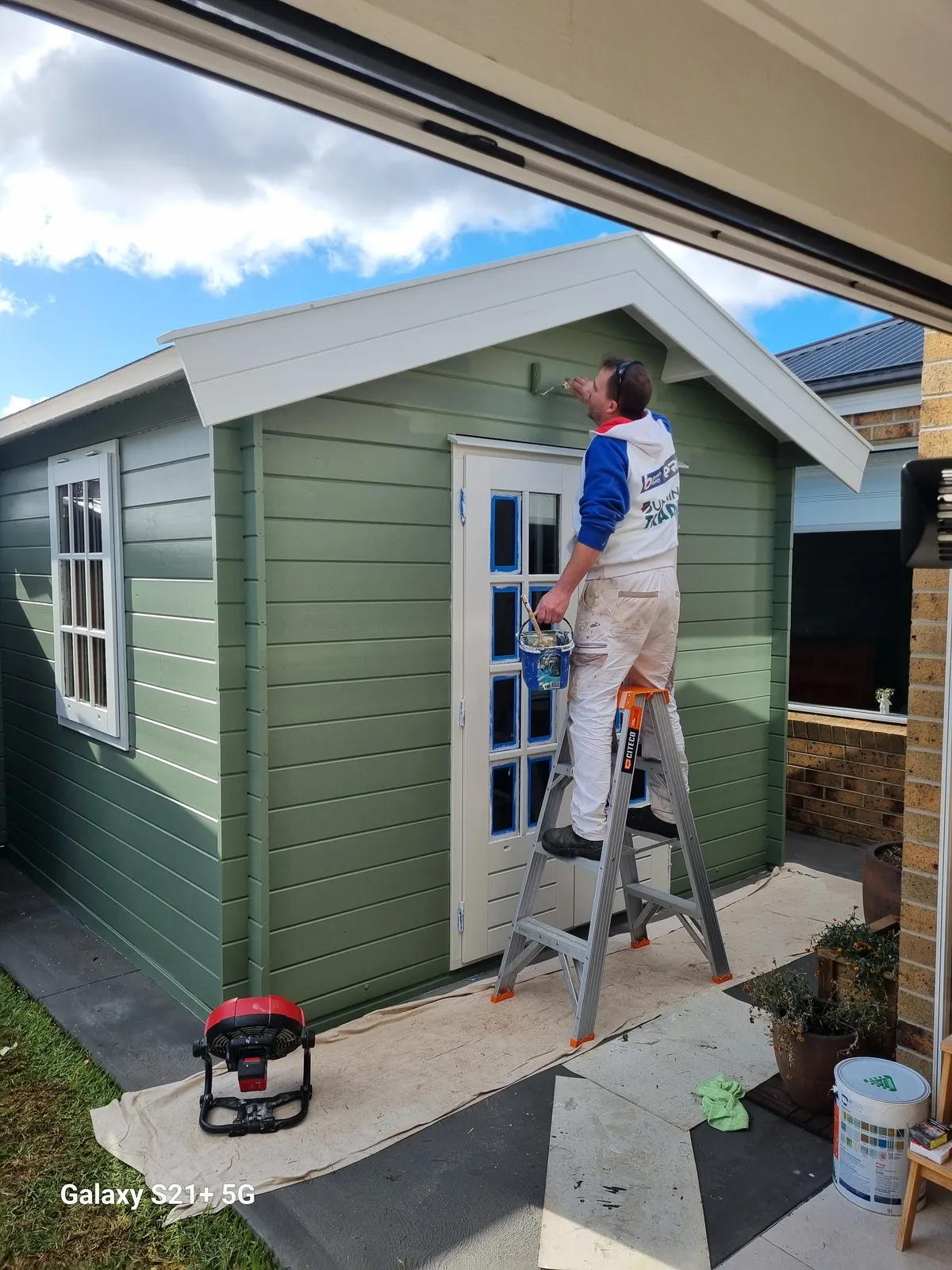 Painter cutting in the sage-green top-coat with crisp white trim around the eaves