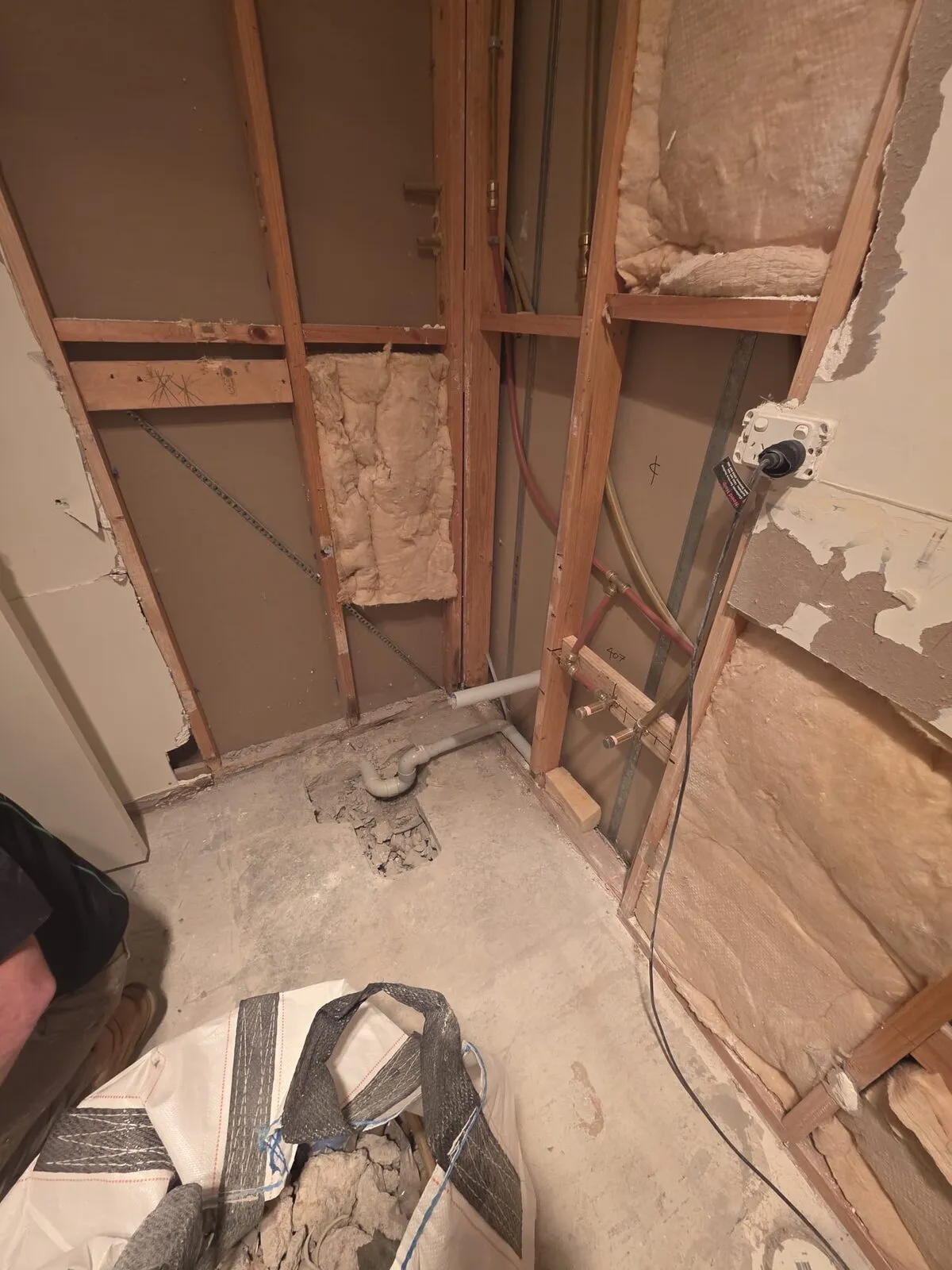 Bathroom stripped back to studs with old plumbing and insulation exposed