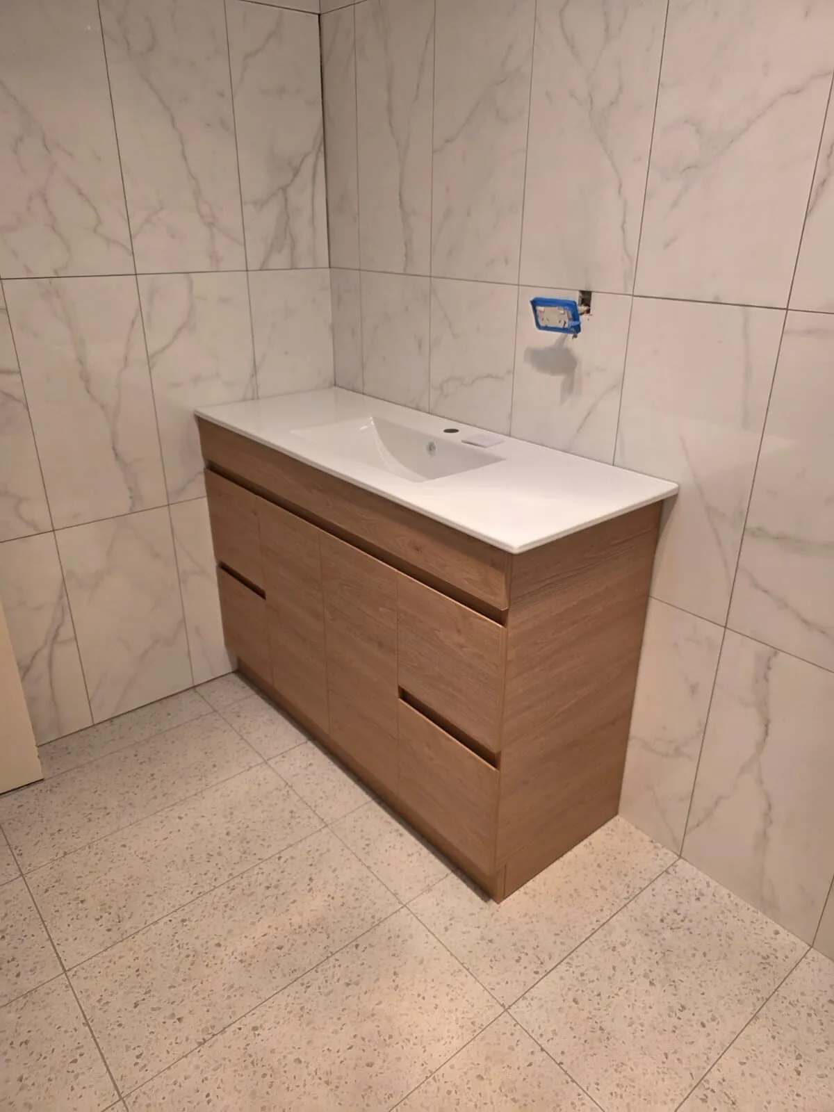New timber vanity with stone top installed against marble-look feature wall